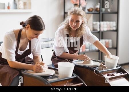 Two female ceramic artists in apron using clay material working in potter studio. Evening freelance distance learning. Adult hobby adventure. Winter Stock Photo