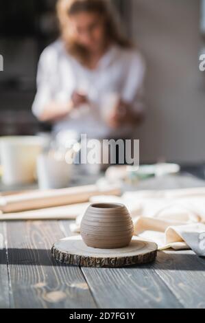 Newly made on a pottery wheel clay pot on a wooden table. Woman paint the ceramic on a background in a pottery studio. Stock Photo