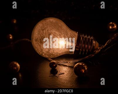 Close up of a light bulb containing tiny white feathers laying on a dark surface decorated with golden glitter balls