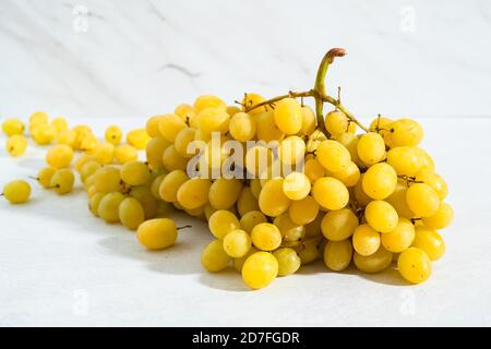 The grape cluster. Seedless golden yellow, sweet and juicy grapes close up on light marble background Stock Photo