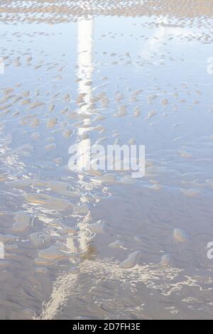 Textures made by water and wind on the sand at the beach, reflections of a windmill and light in the water Stock Photo