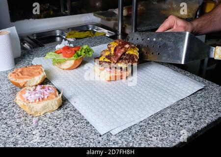 Man cooking american big burger with cheddar, ketchup, hamburger in pandemic times Stock Photo