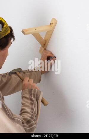 A man hangs a shelf in an apartment on a white wall, a worker scores plastic anchor with a hammer Stock Photo