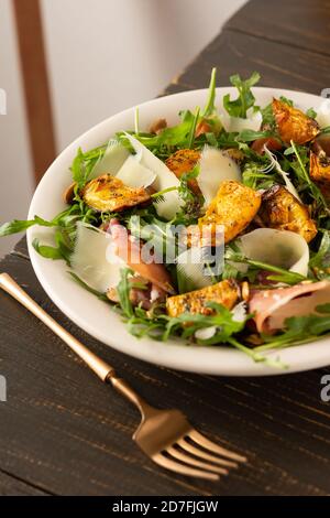 Light autumn salad with arugula, baked pumpkin, prosciutto and young parmesan, a plate of salad on a wooden table