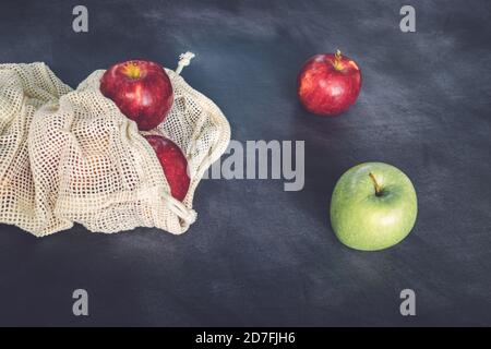 Red and green apples in cotton mesh eco bag on a dark background. Sustainability and Zero waste shopping concept. Top view Stock Photo