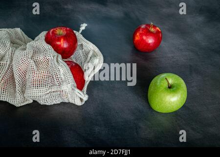 Red and green apples in cotton mesh eco bag on a dark background. Sustainability and Zero waste shopping concept. Top view Stock Photo