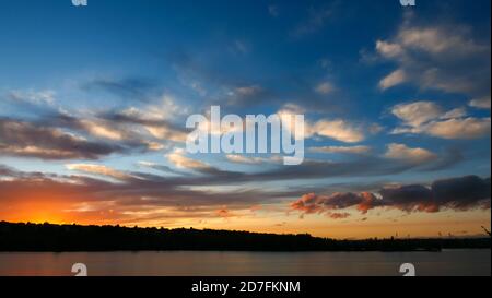 Amazing sunset over the water. Beautiful landscape with a lake and dramatic sky with cumulus clouds on the horizon. Stock Photo