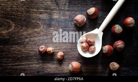 Nuts on a wooden table. Hazelnuts in the shells and shelled. A wooden spoon and nuts on brown table. Stock Photo