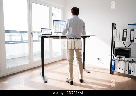 Man Working On Computer At Standing Desk In Home Office Stock Photo