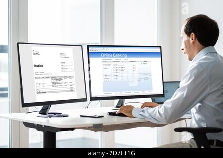 Young Businessman Looking At Invoice While Doing Online Banking On Computer Stock Photo