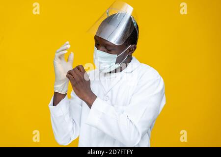 african medical personnel wearing lab coat, face mask and shield, adjusting his surgical gloves