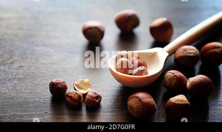 Nuts on a wooden table. Hazelnuts in the shells and shelled. A wooden spoon and nuts on brown table. Stock Photo