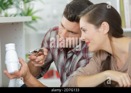 woman looking at male plumber repairing sink pipe in kitchen Stock Photo