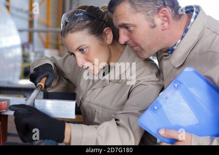 woman filing metal supervisor watching over her shoulder Stock Photo