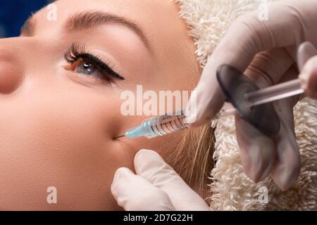 The beautician gives an injection of hyaluronic acid into the cheekbones. Injections of skin rejuvenation. Stock Photo