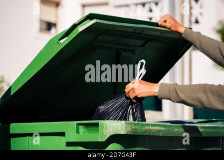 Man throwing out black eco-friendly recyclable trash bag in to big plastic green garbage container. Take out the trash Stock Photo