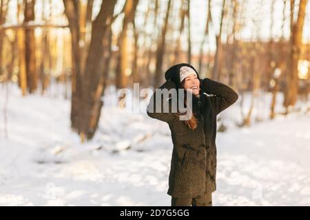 Winter snow fun happy girl walking outside in cold weather protecting ears holding wool hat over ears active outdoor lifestyle. Asian girl wearing Stock Photo