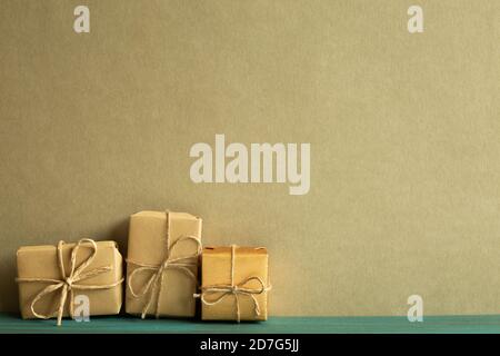Gift boxes wrapped in kraft paper on wooden table with khaki green background. Anniversary, birthday, christmas concept Stock Photo