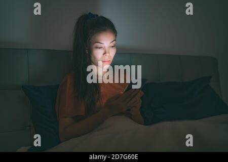 Phone in bed - tired asian woman staying up late at night using mobile cellphone addicted to social media smartphone unable to sleep awake from Stock Photo