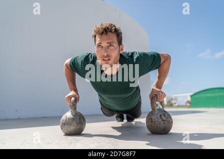 Training fit man exercising pushup exercises on kettlebell weights in gym. Fitness athlete strength training body core doing push-ups holding on Stock Photo