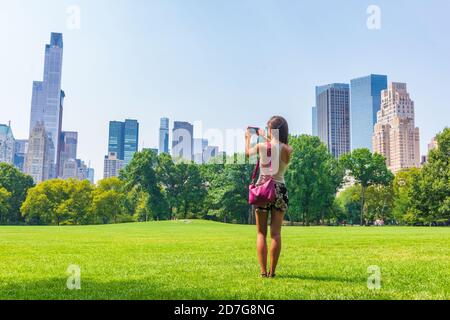 New York City woman tourist taking photo with phone of NYC Skyline in Sheep Meadow Central Park. Summer travel vacation landscape manhattan walk Stock Photo