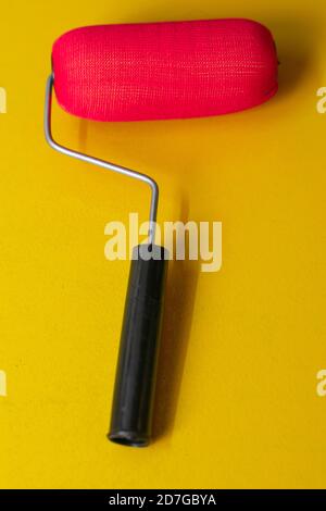 Red paint roller with black handle on yellow background Stock Photo