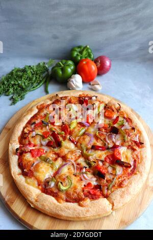 Food- Traditional Italian veggie pizza. Toppings are capsicum, corn, tomatoes, onion, red chilies, and cheese. Ingredients and vegetable background Stock Photo