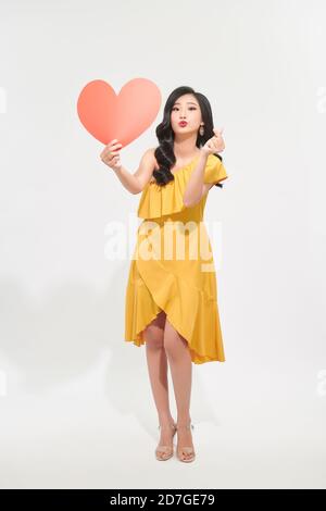 dreamy girl holding in hands big paper heart sending air kiss isolated on bright  color background Stock Photo