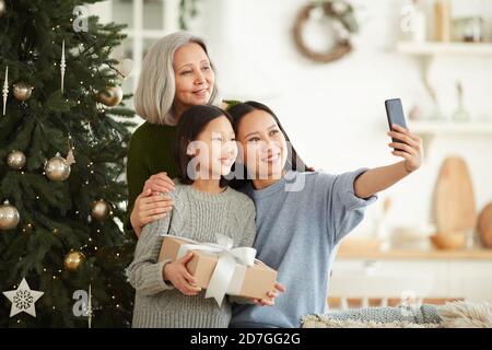 Asian family of three making selfie portrait on mobile phone standing near the Christmas tree during holiday Stock Photo