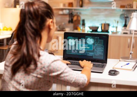Hacker woman launching a cyberattack on bank firewall from home during night time. Programmer writing a dangerous malware for cyber attacks using performance laptop during midnight. Stock Photo