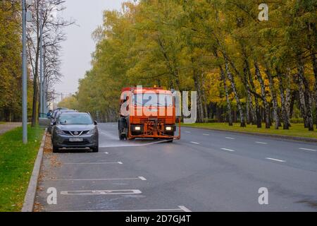 Moscow. Russia. October 11, 2020. An orange heavy truck washes autumn leaves off the asphalt street. The work of public utilities in the city. Autumn Stock Photo