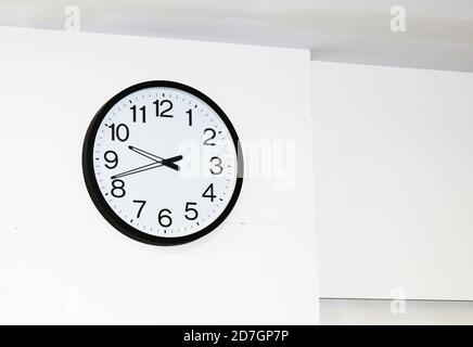 Large wall clock with white face, black border, stylish black hands and clear black numerals on a white wall Stock Photo