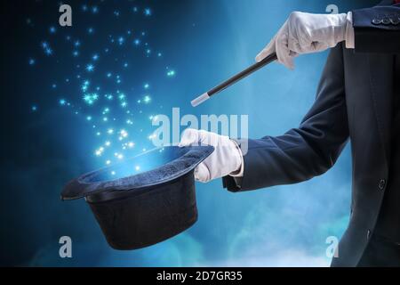 Magician or illusionist is showing magic trick. Blue stage light in background. Stock Photo