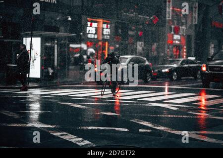 Raining road with traffic lights at night. City life on a rainy day. Drops of rain stopped in motion against lights of cars, bikes, and people walking Stock Photo