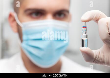 Doctor holding an ampoule for vaccination or beauty treatment in his hand - focus on the ampoule Stock Photo
