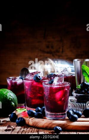 Alcoholic cocktail Darkside, with liqueur, blueberry, lime juice, crushed ice, bar tools on a vintage wooden background, selective focus Stock Photo