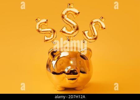 Golden piggy bank on yellow background with Gold USD Sign Balloons. Golden currency symbol made of inflatable foil balloon. Investment and banking Stock Photo