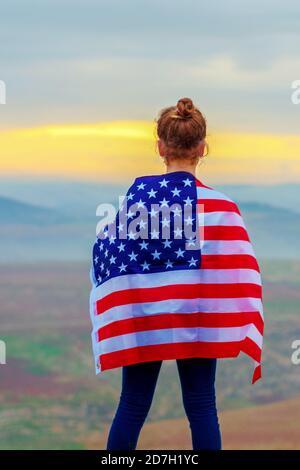 Young little girl holding flag of America USA at sunset outdoors. Stock Photo
