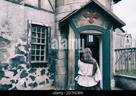 A woman parishioner in a headscarf stands and crosses herself at the door of a retro american church Stock Photo