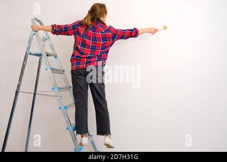 The woman paints the wall brush standing on a stepladder, copy space Stock Photo