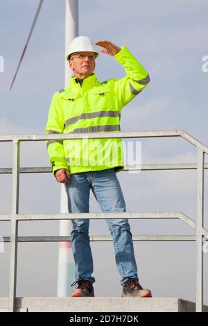 Mature engineer looking out for a green future in front of a wind turbine - focus on the person Stock Photo