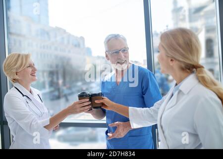 Smiling medical workers drinking coffee, having friendly conversation Stock Photo