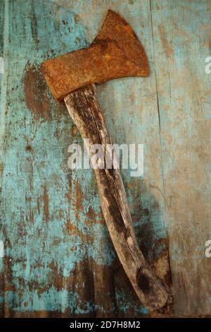 an old rusty ax lies on the blue shabby table. Stock Photo