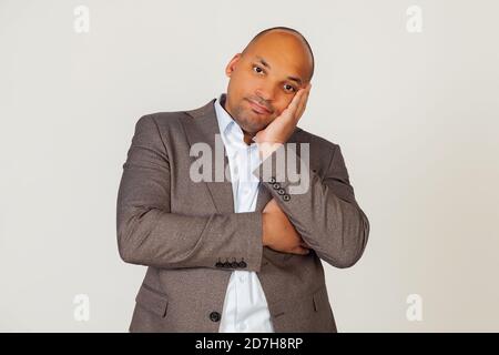 Portrait of a young african american guy businessman holding his hand on his face and staring indifferently at the camera, thinks he looks tired and depressed with crossed arms. gray background. Stock Photo