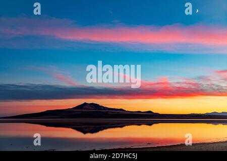 The image of Antelope Island reflects on the water of the Great Salt Lake as the sunset afterglow reflects in the clouds above. Stock Photo