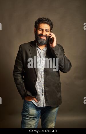 Young Indian man, in a blazer and denims, talking on his phone Stock Photo