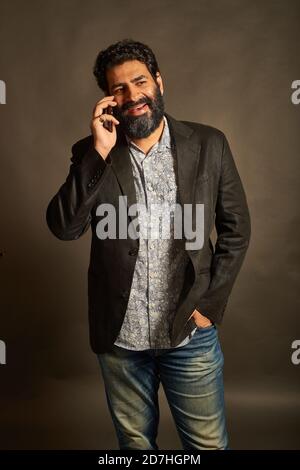 Young Indian man, in a blazer and denims, talking on his phone Stock Photo