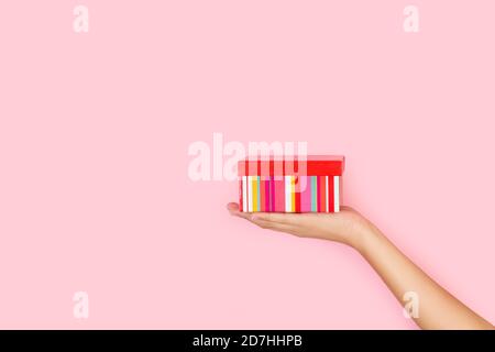 Woman hand holding a striped box on a pink background with copy space Stock Photo