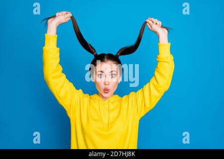 Photo of funny pretty lady hold raise two long tails arms good mood amazed fast growth hair wear casual yellow hoodie pullover isolated bright blue Stock Photo