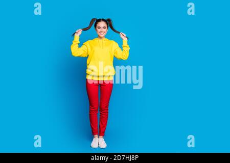 Full length photo of cheerful funny lady hold two tails arms good mood playful wear casual yellow hoodie pullover red trousers sneakers isolated Stock Photo